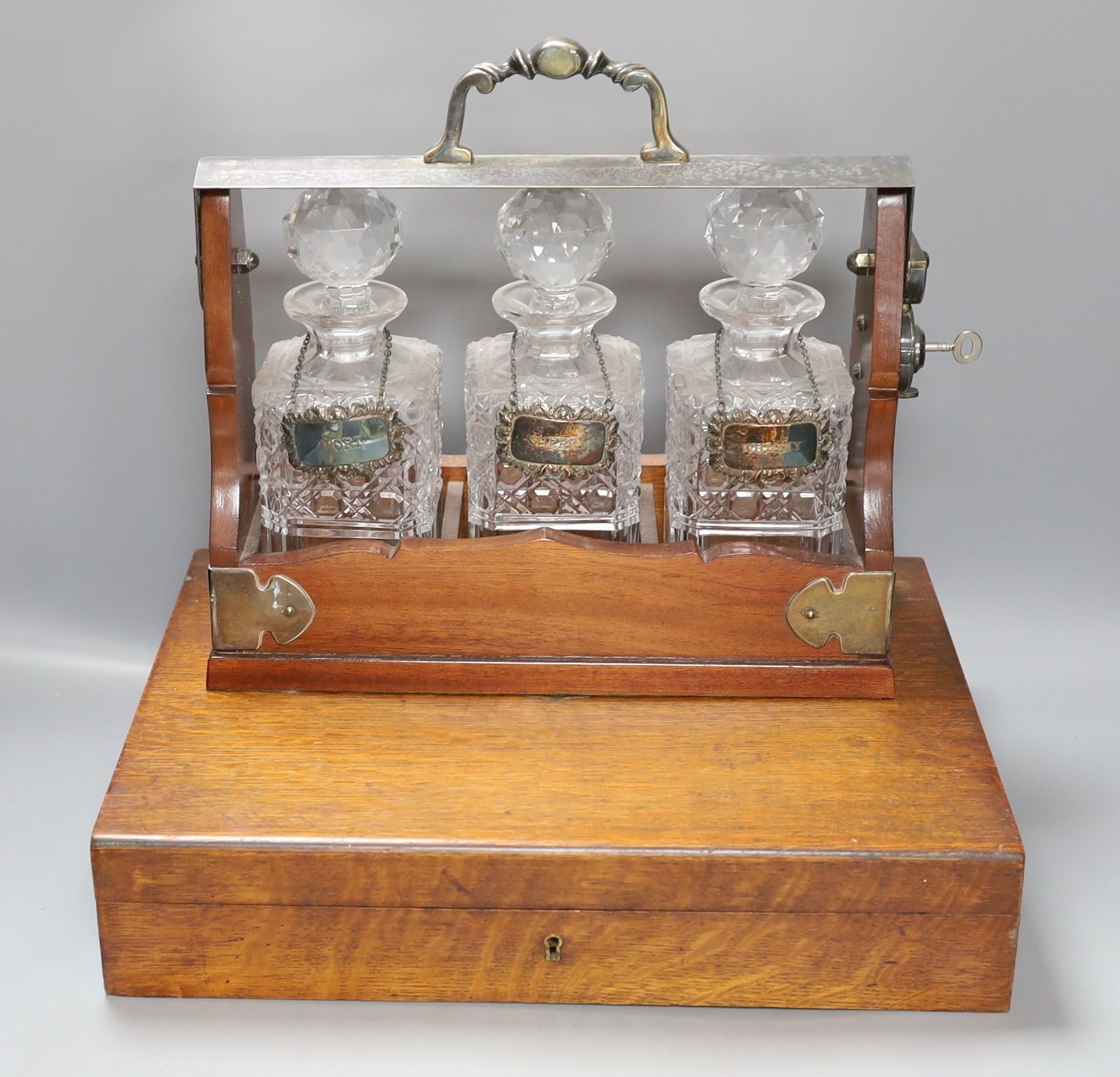 A three decanter tantalus - with labels, together with an oak canteen of table plated cutlery